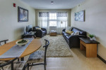 Living room of a furnished apartment with modern decor, large windows, and cozy seating area.