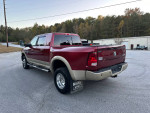 2012 Ram 3500 Mega Cab Laramie Longhorn Diesel in red parked on a road, showcasing its size and towing capability.
