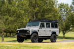 1993 Land Rover Defender 110 in Nardo Grey, restored with black leatherette interior, parked in a scenic setting.
