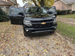 2021 Chevrolet Colorado LT 4WD parked outside, featuring a black exterior and open doors, surrounded by autumn leaves.
