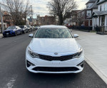 Front view of a 2019 Kia Optima LX sedan in pearl white parked on the street, showcasing its clean design and modern features.