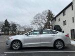 Side view of a 2013 Ford Fusion SE sedan in silver color parked outside, showcasing its clean body and wheels.