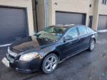 2011 Chevrolet Malibu LT in black with 65,000 miles parked in front of a garage.