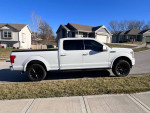 2020 Ford F150 Lariat in white, parked on the street with modern homes in the background.