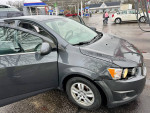 2013 Chevrolet Sonic LT Hatchback parked at a gas station, showing minor damage on the front bumper.