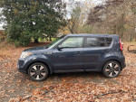 2016 Kia Soul in blue with leather seats, parked among autumn leaves, showcasing its modern design.