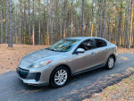 Silver 2012 Mazda 3 i Grand Touring FWD parked on a forest road with pine trees in the background.