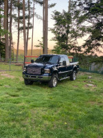 2006 Ford F350 Lariat 4WD truck in blue parked on grass, showing some rust but well-maintained.