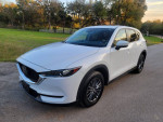 2019 Mazda CX-5 Touring in white, parked on road with greenery in background, showcasing modern design and features.