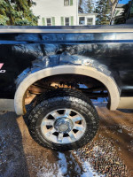 Close-up view of the wheel well and tire of a 2008 Ford F350 King Ranch with noticeable body rust.
