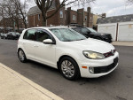 2011 Volkswagen GTI hatchback in white, showcasing its sleek design and shiny wheels on a city street.