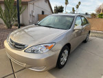 2004 Toyota Camry in champagne metallic, clean with low mileage, parked in front of a house.