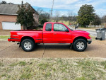 Red 2003 Toyota Tacoma V6 SR5 parked on a driveway, showcasing clean exterior and modern tires.