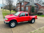 2003 Toyota Tacoma V6 in red with 137,000 miles parked outside a house