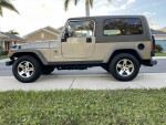 2005 Jeep Wrangler Rubicon 4WD in Light Khaki Metallic parked on a street with grass, perfect for off-roading enthusiasts.