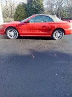 1994 Ford Mustang GT convertible, red with a new top, parked on a driveway, showing low mileage and stock condition.