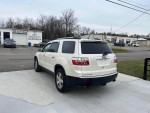 2010 GMC Acadia in pearl white with black leather, parked outside a car repair shop.