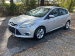2013 Ford Focus S FWD in silver, 150,000 miles, well maintained, with cloth interior and cracked windshield.