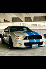 White Shelby GT500 with blue stripes parked in a modern garage setting