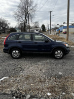 2009 Honda CR-V in dark blue, parked on gravel with trees in background, showcasing its clean exterior and spacious design.