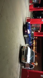 Two cars at a gas station, featuring a 2006 Monte Carlo with a V6 engine and a nearby blue vehicle.