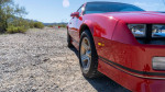 Close-up of a red 1988 Chevrolet Camaro IROC showcasing its sleek design and wheel on a gravel road