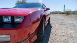 Close-up of a red 1988 Chevrolet Camaro IROC showcasing its headlights and wheel on a gravel road
