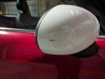 Close-up of the side mirror of a red MINI Cooper showcasing minor wear and tear.