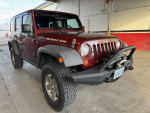 2010 Jeep Rubicon Unlimited in red, displaying custom bumpers and rugged tires in a garage setting.