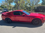 2010 Ford Mustang GT in red with aftermarket wheels and modifications, parked on a residential street