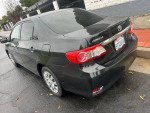 2012 Toyota Corolla LE in black with low mileage, parked on a wet street, showcasing its sleek design.