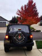 Rear view of a 2011 Jeep Wrangler Sport parked outdoors, showcasing new LED headlights and a compass spare tire cover.