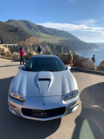 Front view of a 2002 Chevrolet Camaro SS parked by the coast with mountains in the background.