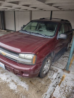 2006 Chevrolet TrailBlazer in maroon color, parked under a shelter with slight dirt on exterior.