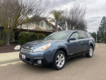 Clean 2013 Subaru Outback 2.5i AWD with manual transmission, parked on the street surrounded by greenery.