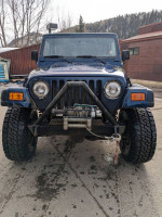 Front view of a blue 2000 Jeep Wrangler Sport 4WD with new tires and aftermarket features.