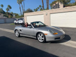 1997 Porsche Boxster convertible in silver with red leather interior parked in a sunny driveway.