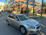 2016 Chevrolet Cruze LS in silver parked on a city street with modern buildings in the background.
