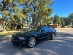 2012 Ford Mustang V6 in black with luxury features parked on a sunny street surrounded by trees