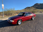 1987 Ford Mustang 5.0 manual hatchback in red with new tires in a desert setting.