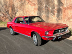 Candy apple red 1967 Ford Mustang with red interior parked near rocky terrain.