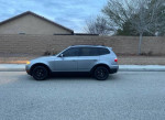 Side view of a 2009 BMW X3 SUV with black wheels, parked on a residential street.