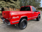 1997 GMC Sierra 1500 SL 4WD in red with black wheels, showing rear view and 4x4 badge