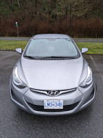 Front view of a 2015 Hyundai Elantra with winter tires parked outdoors, showing sleek design and clear headlights.