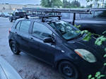 2007 Toyota Yaris hatchback, black, with roof rack, parked in a lot, showing winter tires