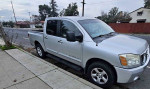 Silver Nissan Titan 4x4 crew cab parked on the street, showcasing its strong build and spacious design.