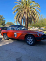 Bright red 1980 MG convertible parked under palm trees, showcasing its vintage style and unique racing number.