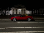 Red 1994 Mazda MX-5 parked on the street at night with a backdrop of a building.