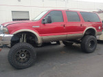 2000 Ford Excursion in red with tan interior, lifted, ready for sale at a towing yard.