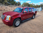 2013 GMC Yukon XL SLT RWD in red, parked on dirt road, showcasing its spacious design and rugged features.